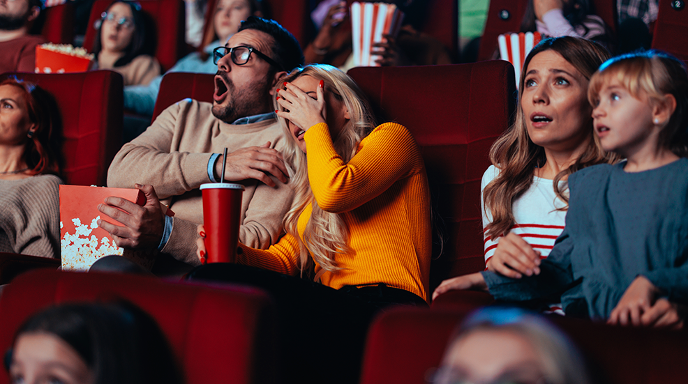 Audience reactions in a cinema including a couple where the man looks shocked and the woman is hiding her face